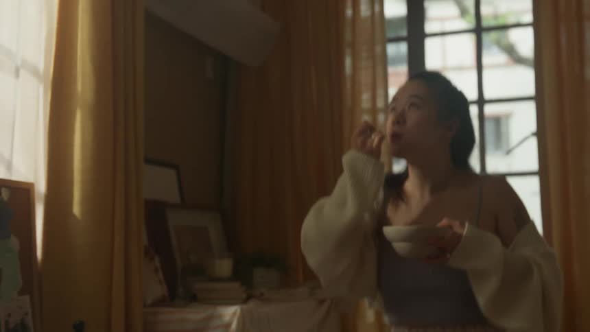 Woman eating cereal while dancing near the window