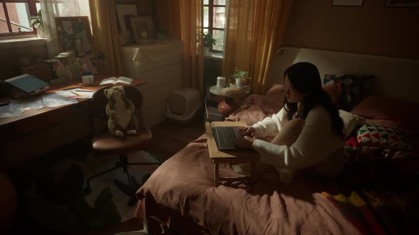 A woman sits on a bed using a laptop on a small tray closes the computer stretches her arms above her head and then relaxes while sitting