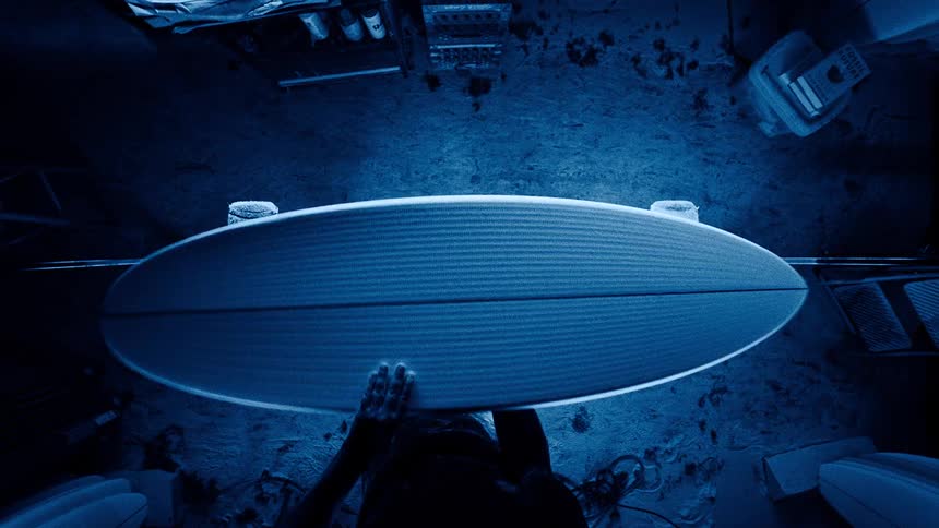 Person shaping a surfboard under intense blue lighting