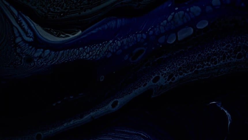 Swirling abstract patterns of blue white and black acrylic paint with organic cell shapes are seen as they slowly move and mix across the frame under bright flashing lights
