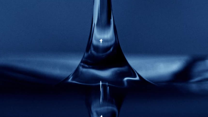 Water droplet suspended above liquid surface creates splashes and ripples in blue tone