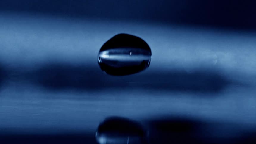A single drop of water falls in super slow motion hitting a still surface and creating a splash