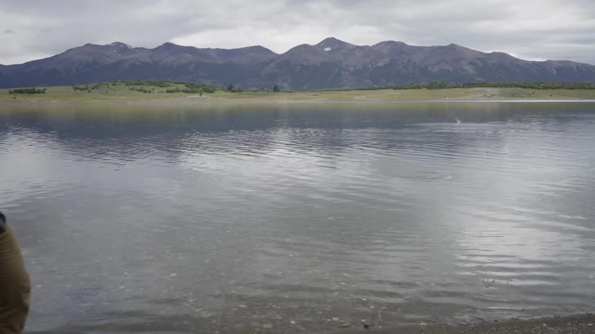A man skips a rock on a mountain lake