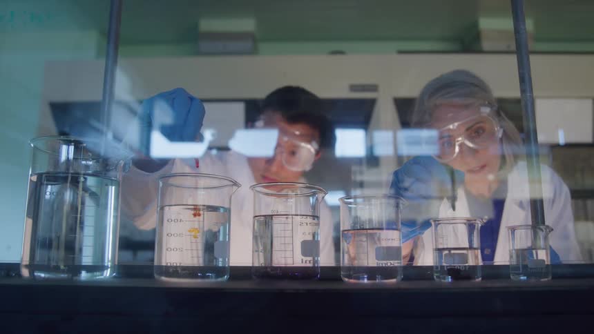 In a laboratory two scientists observe a chemical reaction as a substance is added to a beaker filled with liquid