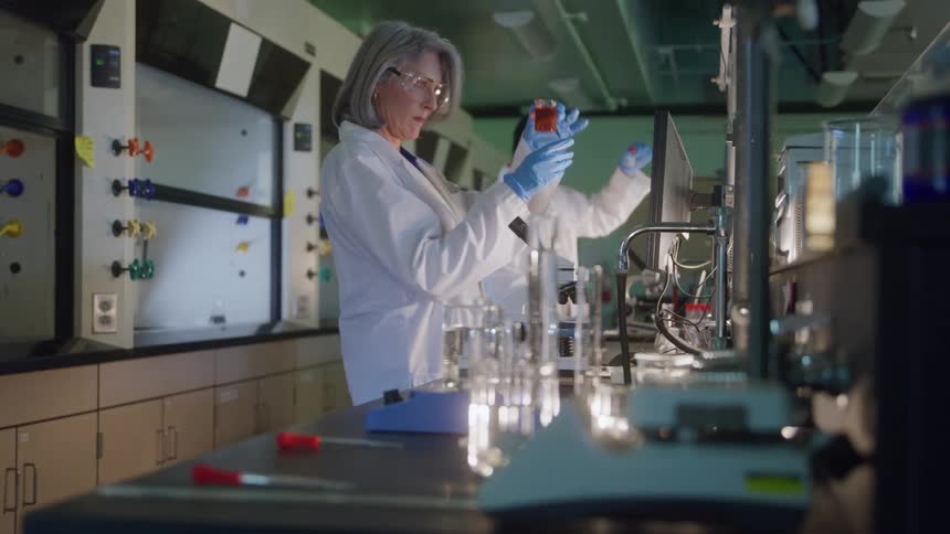 Man and woman handling red liquid in a laboratory equipped with scientific instruments and computers