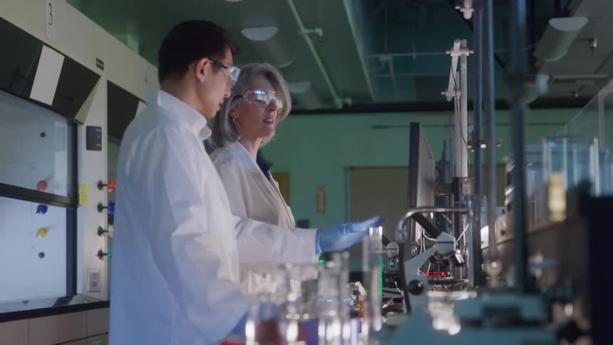 Two scientists in lab coats talking beside a microscope in a laboratory