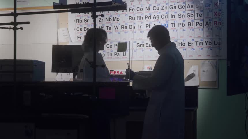 Silhouette of a male scientist talking with a female scientist and taking notes in a lab indoors
