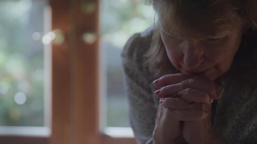 Person with light brown hair leans forward with hands clasped near a window with natural light