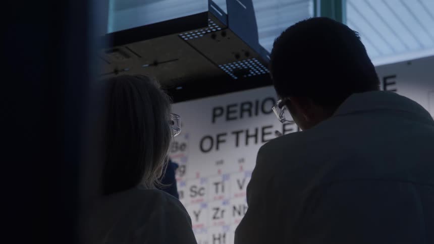 Two scientists talking in front of a periodic table in the laboratory