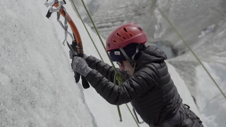 A mountain climber attaches their climbing tools into a snowy mountainside