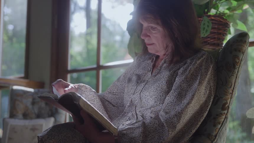 The woman is sitting at home reading a book