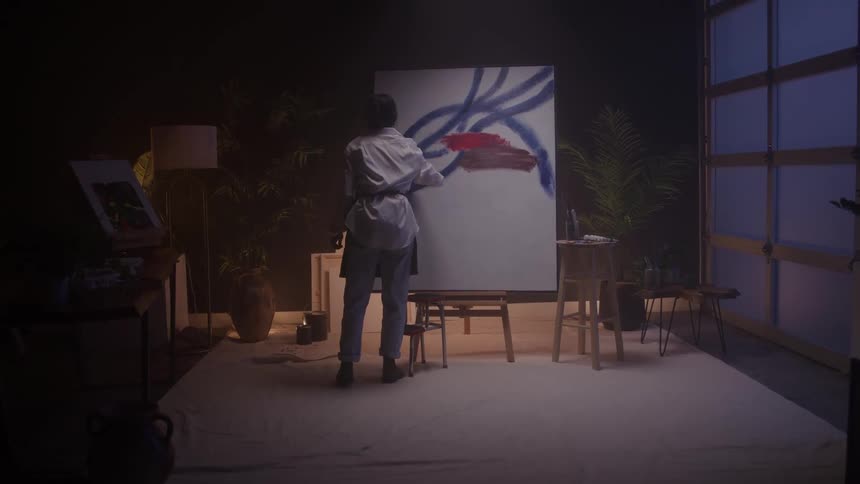 A young female artist painting a large canvas in a room