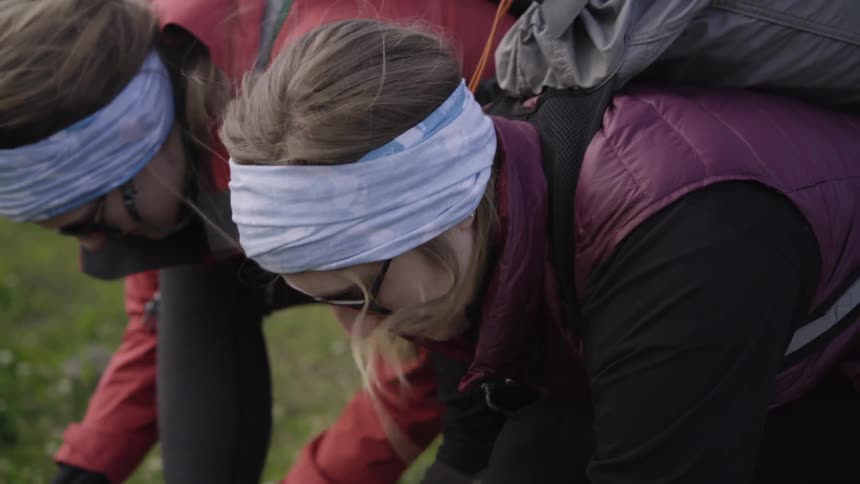 Two backpackers digging in a grassy field on a windy day