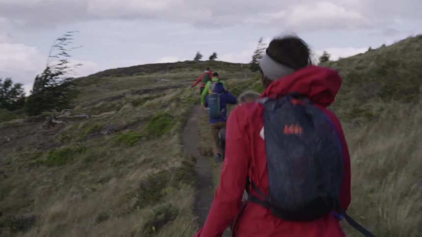 Group of people hiking on hillside trail on windy day