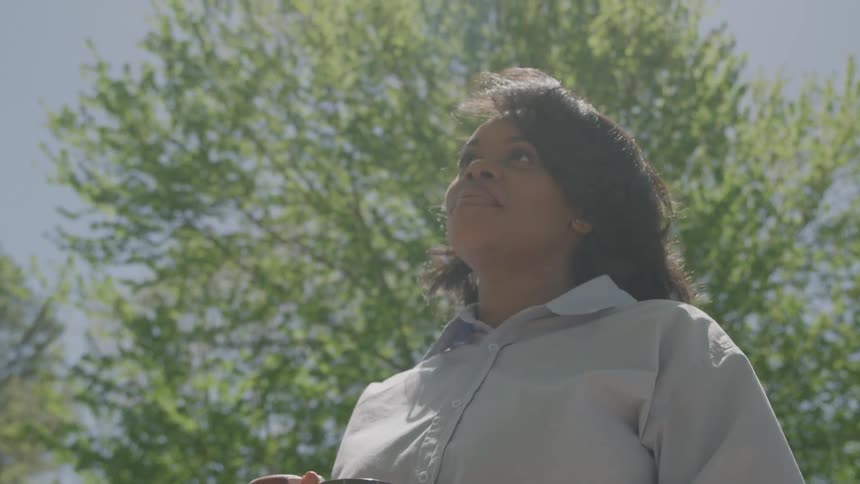 Woman holds a checkered mug with both hands in an outdoor setting under a blue sky with lush greenery in the background