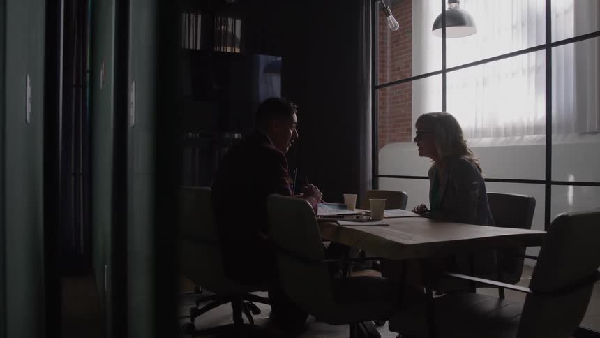 Woman and man sit at a table in a modern glasswalled meeting room