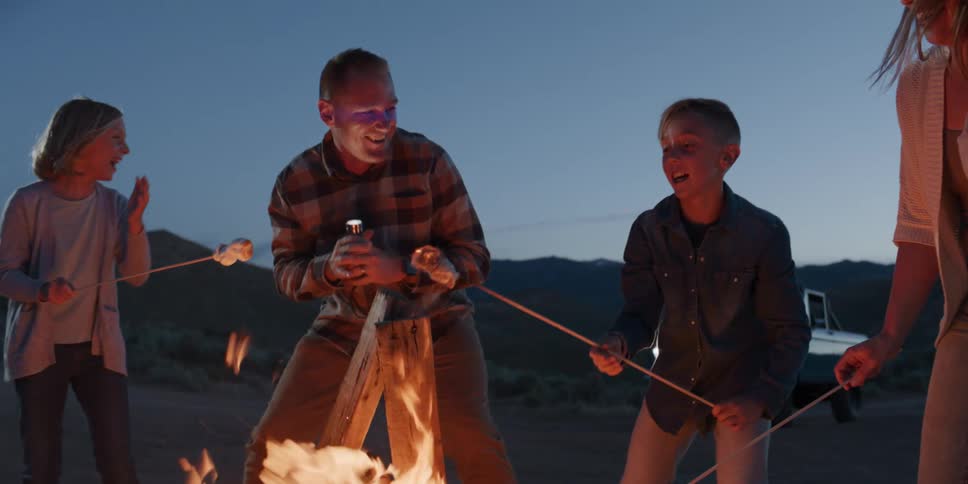 A smiling family of fourfather mother son and daughtergathers around a campfire joyfully roasting marshmallows together under the open sky
