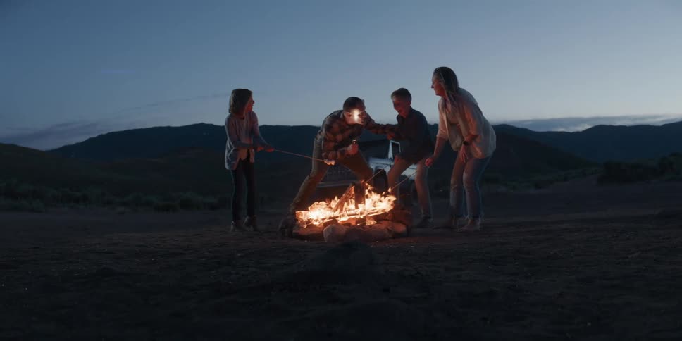 The father is telling a scary story to his family at the campfire
