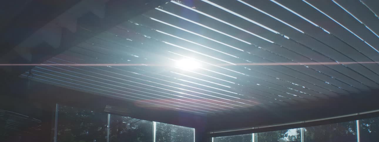 A bright sunlight shines through a modern metal pergola