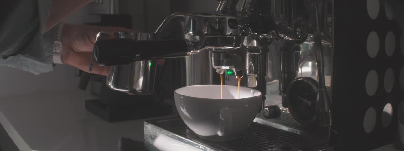 Barista making hot espresso shot from coffee maker machine on counter at cafe