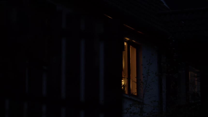 Tracking shot reveals warm light illuminating the interior of a house at night