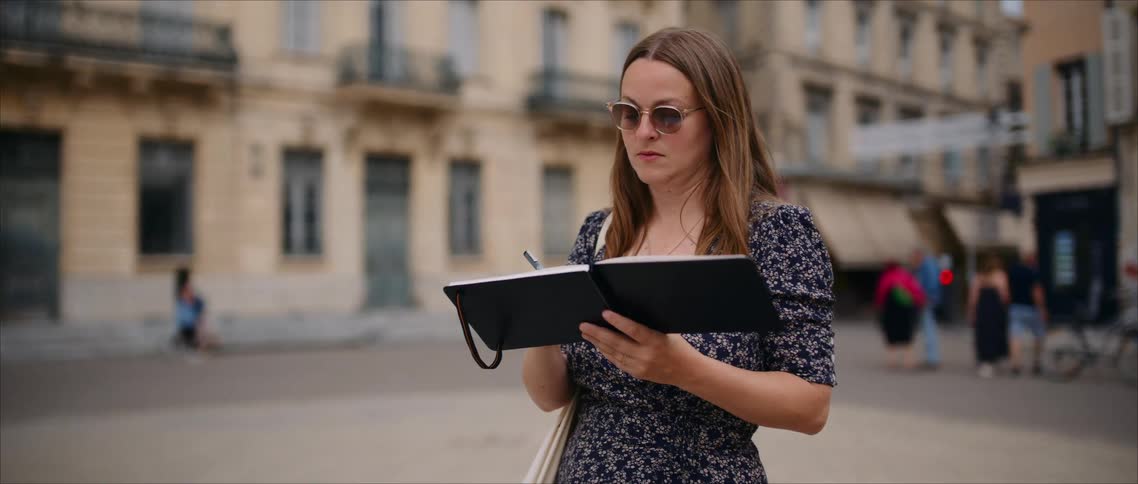 A woman noting in a book while standing in the middle of a city street