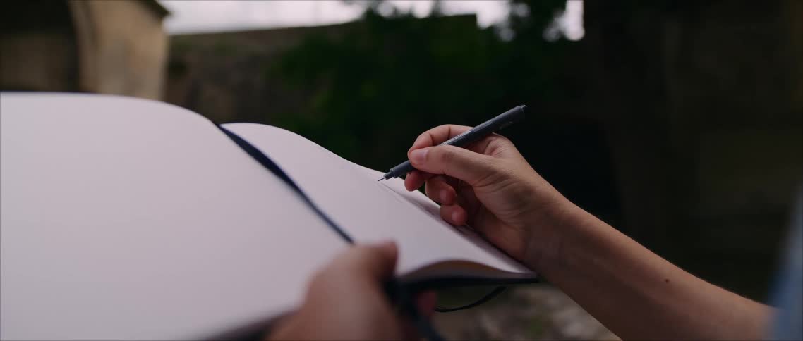 The woman is writing in a notebook outside