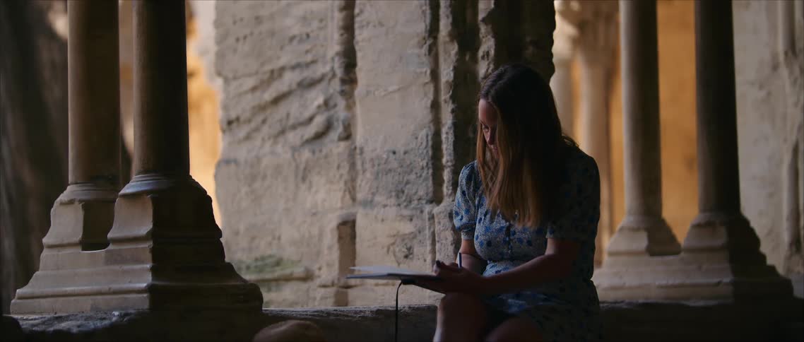 Sketch artist seated in historic ruins captures details in notebook under soft evening light