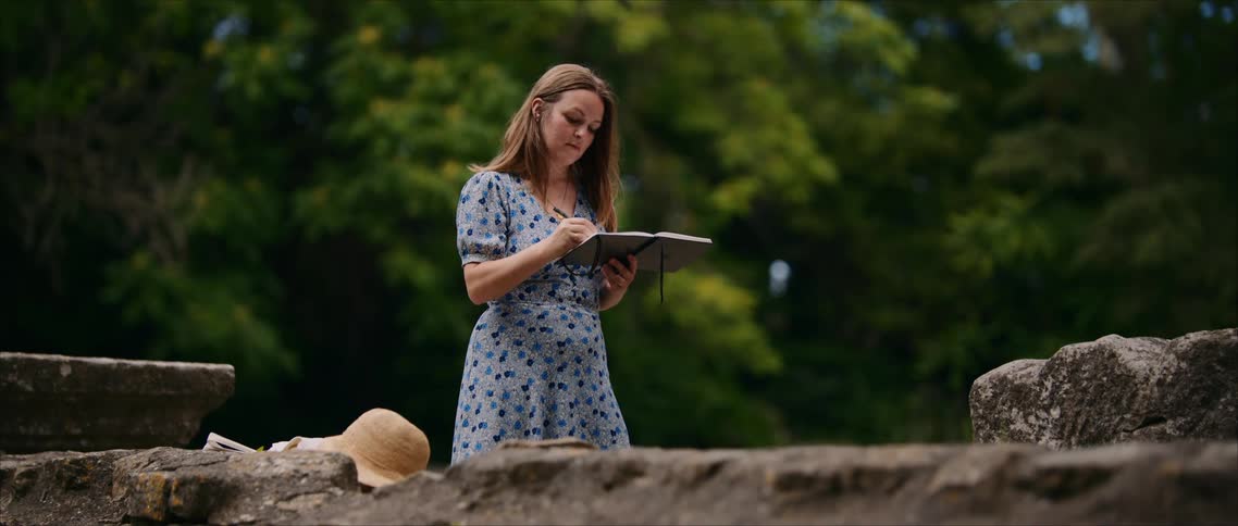 Woman sketching in a notebook outdoors among stones and greenery