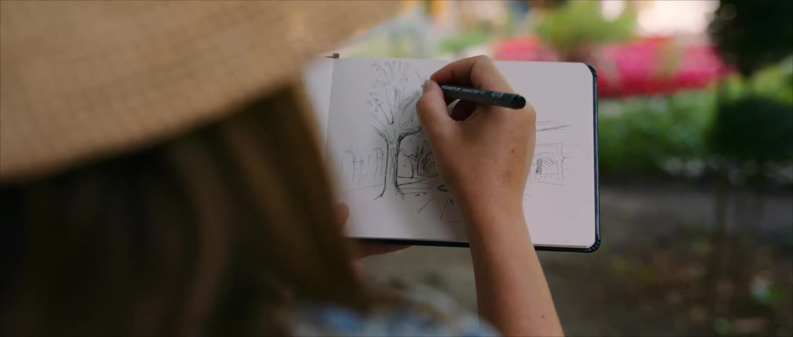 Woman in straw hat sketches natural scene in notebook surrounded by flowers and greenery in sunlit garden