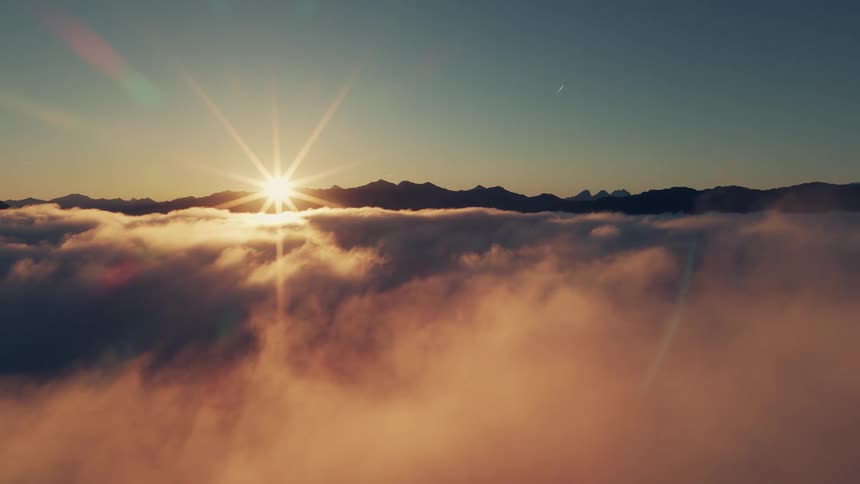 Sun rising above mountains covered by a sea of clouds