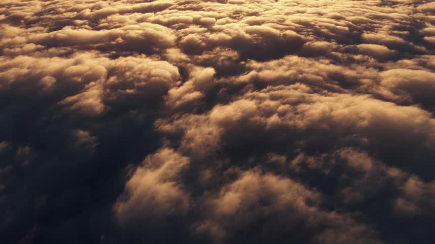 An aerial view looking down shows a dense blanket of dark textured cumulus clouds illuminated with a golden orange glow from the sun setting or rising above them