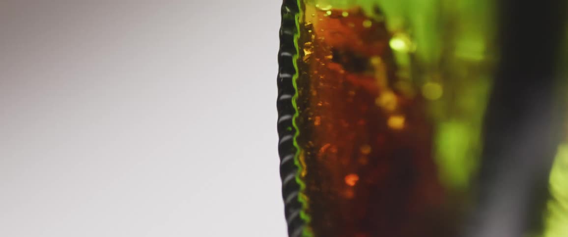 Close up of a red drink rotating horizontally in a green glass bottle