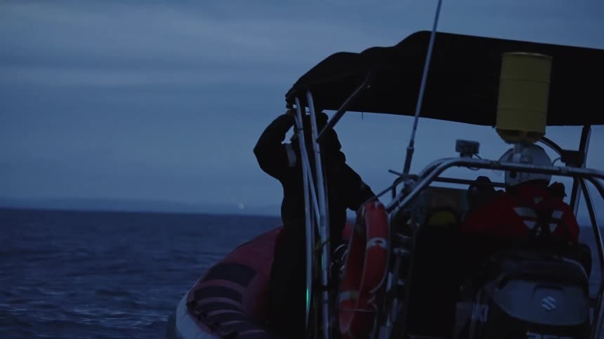 Inflatable boat with outboard motor moves through calm waters at twilight with two crew members onboard