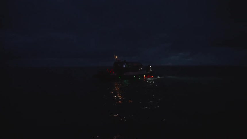 Lit boat floats on dark waters as a mysterious light glows near the surface hinting at nighttime activity