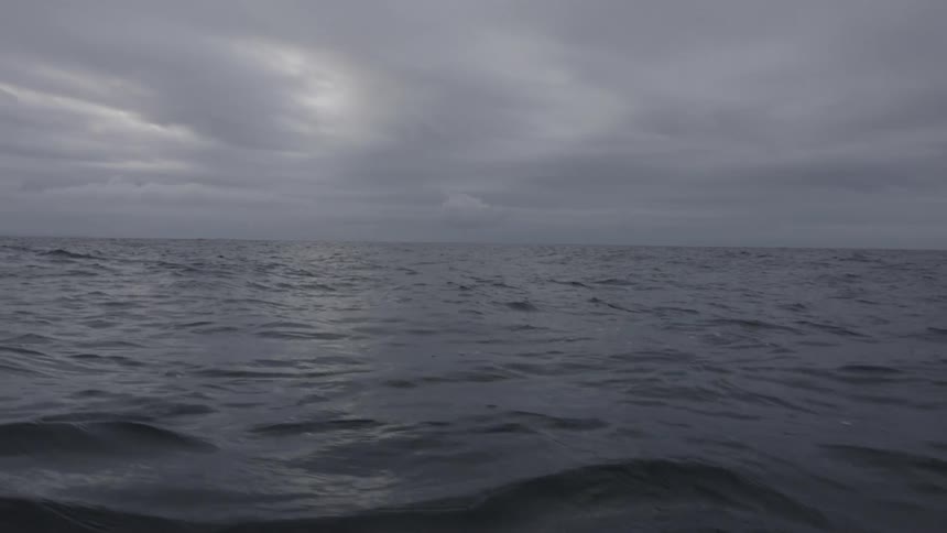 A view from the deck shows large dark gray ocean waves surging and moving under a heavy overcast dark gray sky
