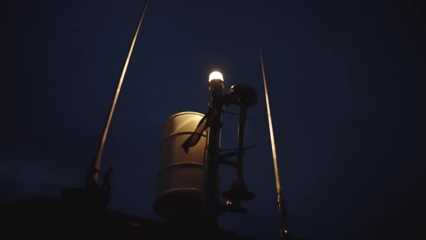 A boat roof carries a glowing mast light with twin antennas and a horn silhouetted against a deep blue night sky