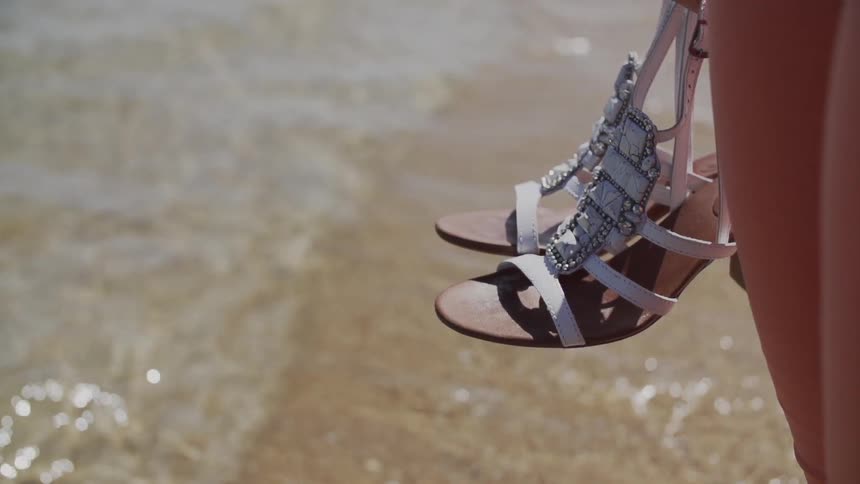 Person carrying sandals near the water