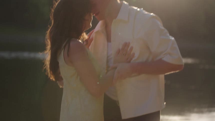 A couple embraces tenderly on a riverbank at sunset