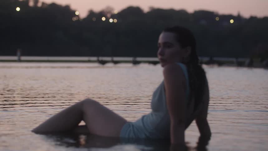 Woman sits by the water at dusk gazing toward the quiet horizon