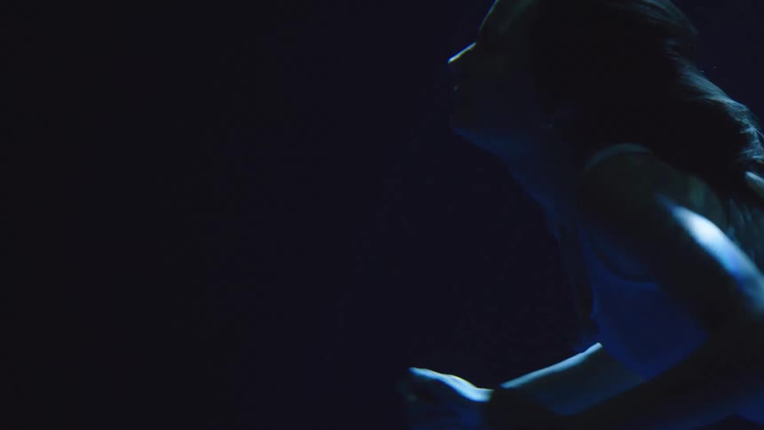 Woman swimming underwater swims upward and surfaces
