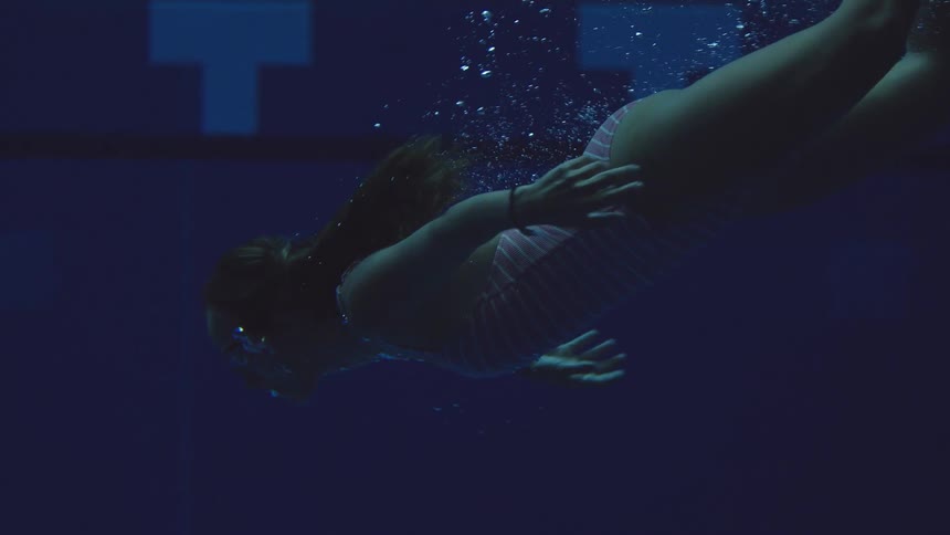 Woman swims underwater in a pool lit by bluish tones