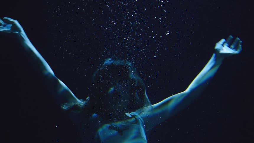 Woman underwater exhales air bubbles as blue light cuts through the water