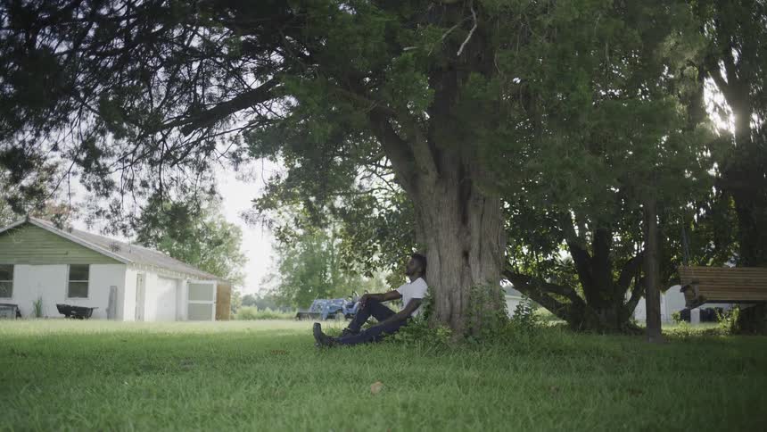 Contemplating man sitting under a large tree on the lawn