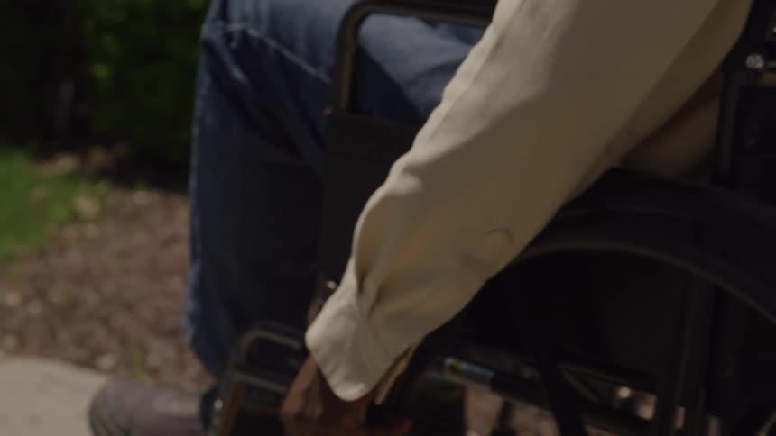 Black man wearing jeans and a brown shirt rolling on a wheelchair outdoors during day time