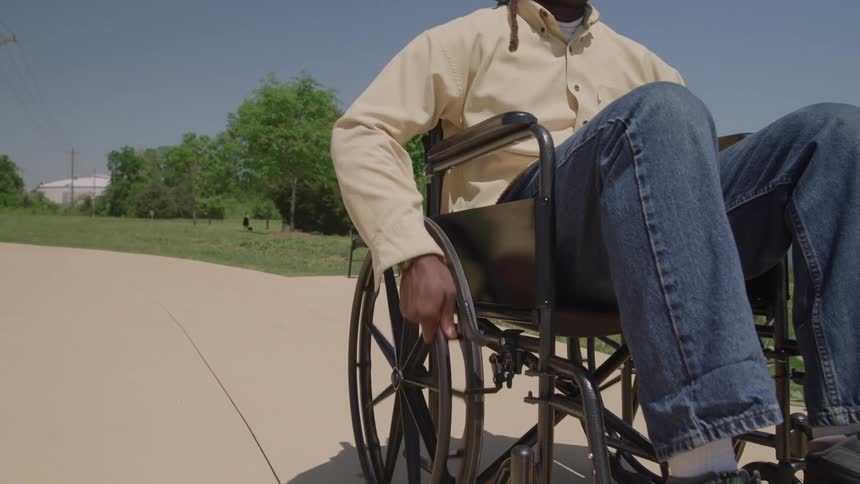 A man propels a wheelchair along a sunny park path