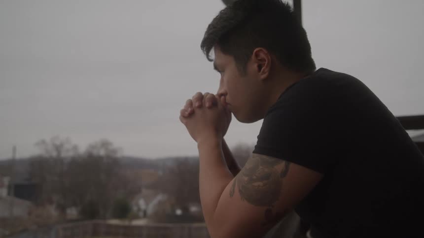 A man leans on a railing contemplatively on a cloudy day