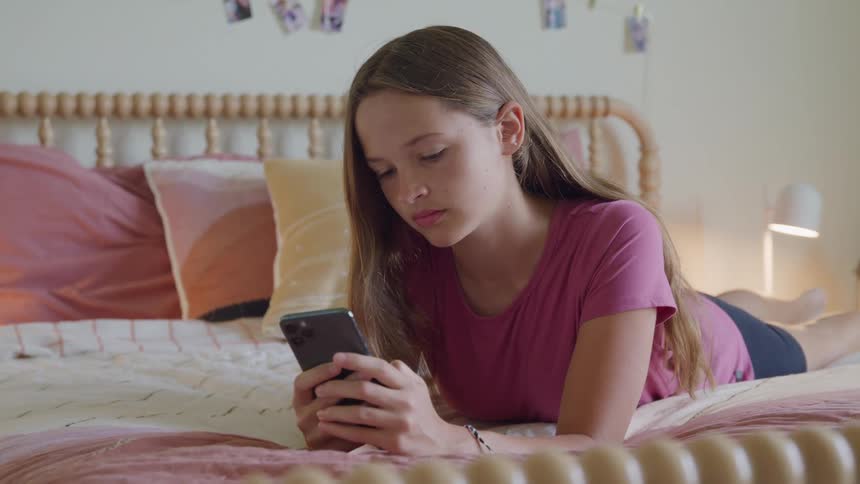 Girl lying on the bed looks at her phone in a room decorated with photos