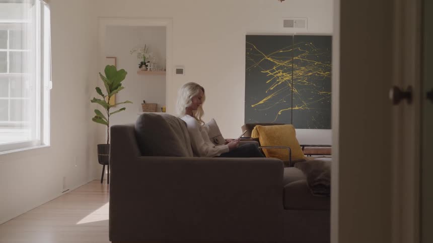 Woman sitting on a sofa uses her phone in a room lit by natural light
