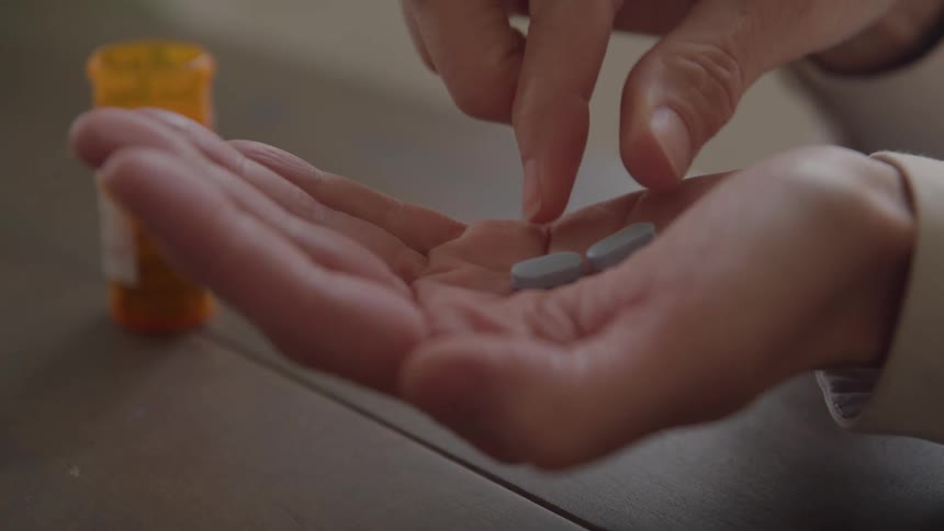 Hand holds pill bottle while the other displays three capsules